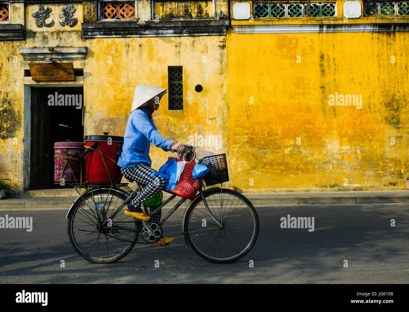 A Vietnamese woman rides a bike in a street in Hoi An, Vietnam Stock Photo