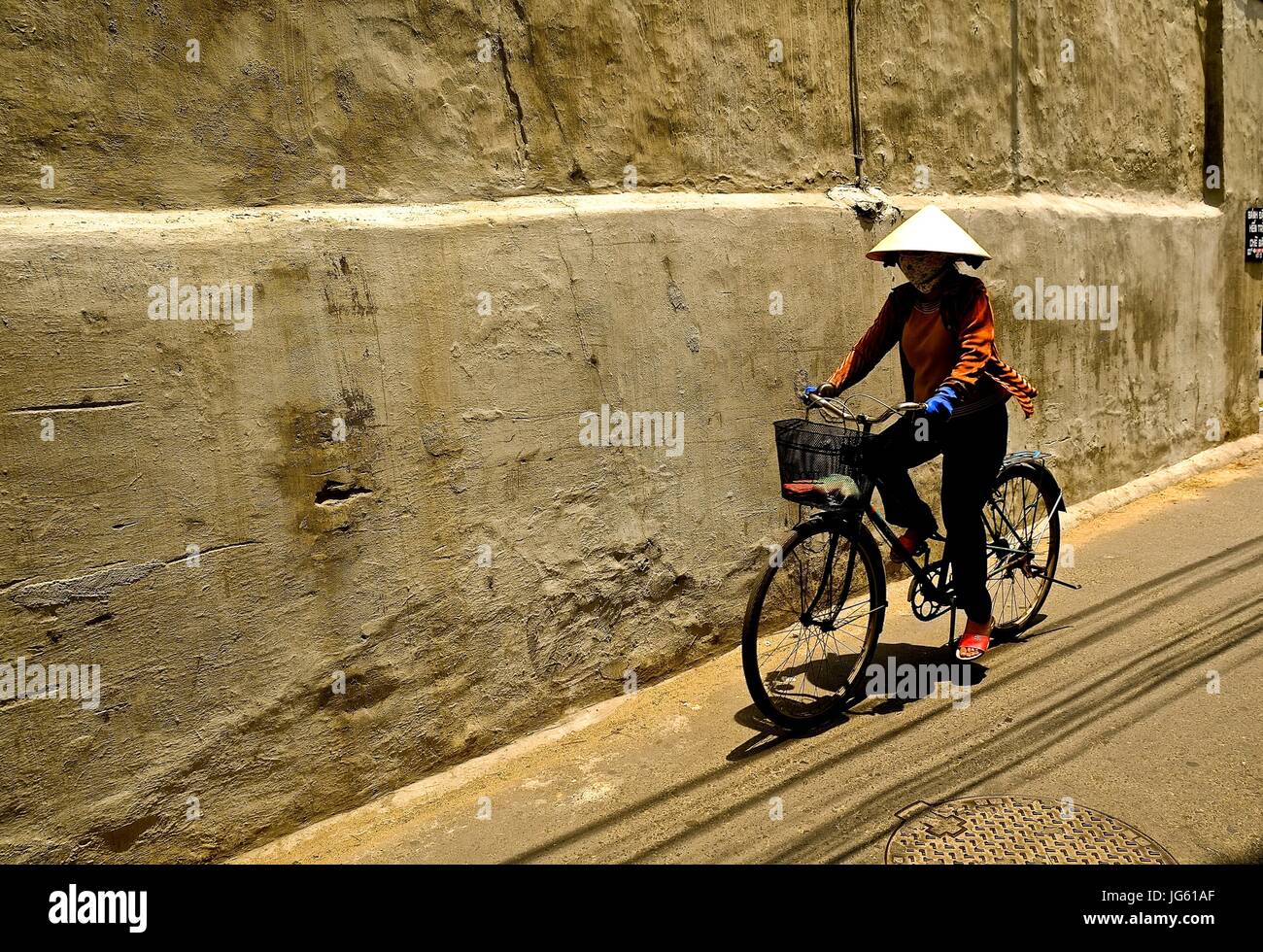 A Vietnamese woman rides a bike in a street in Hoi An, Vietnam Stock Photo