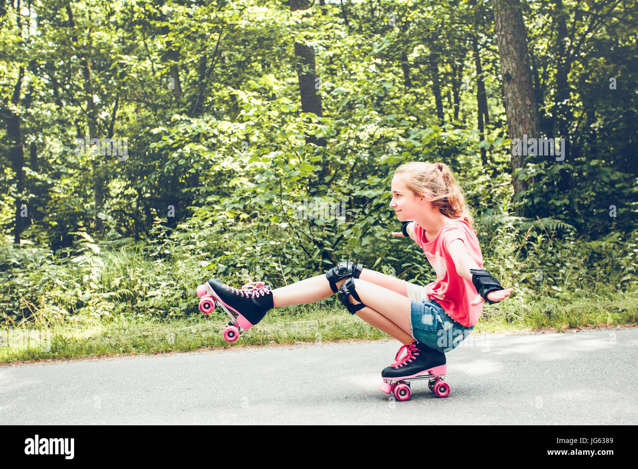 Young girl roller skating down on a forest road on summer day Stock Photo