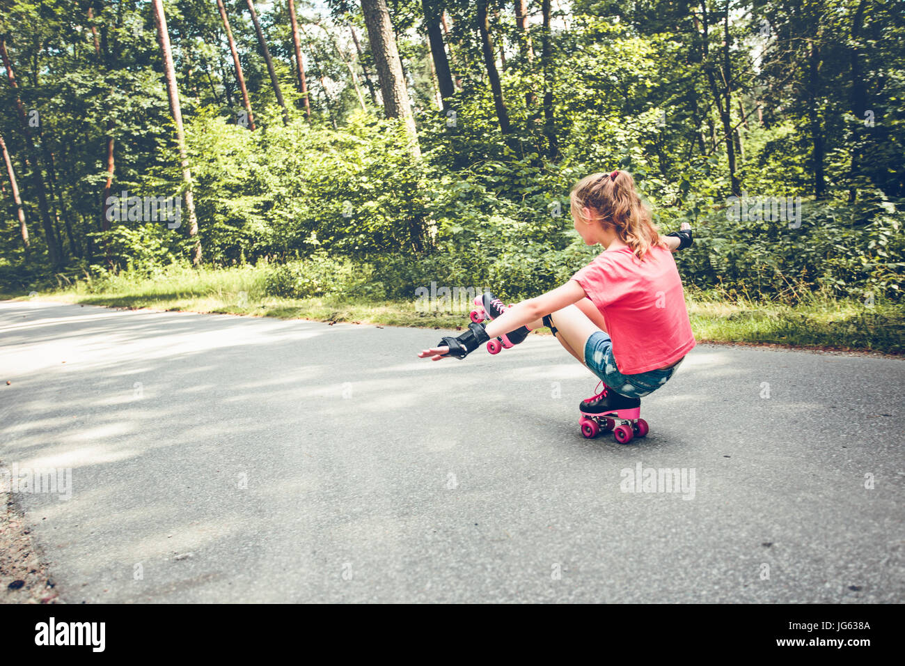 Young girl roller skating down on a forest road on summer day Stock Photo