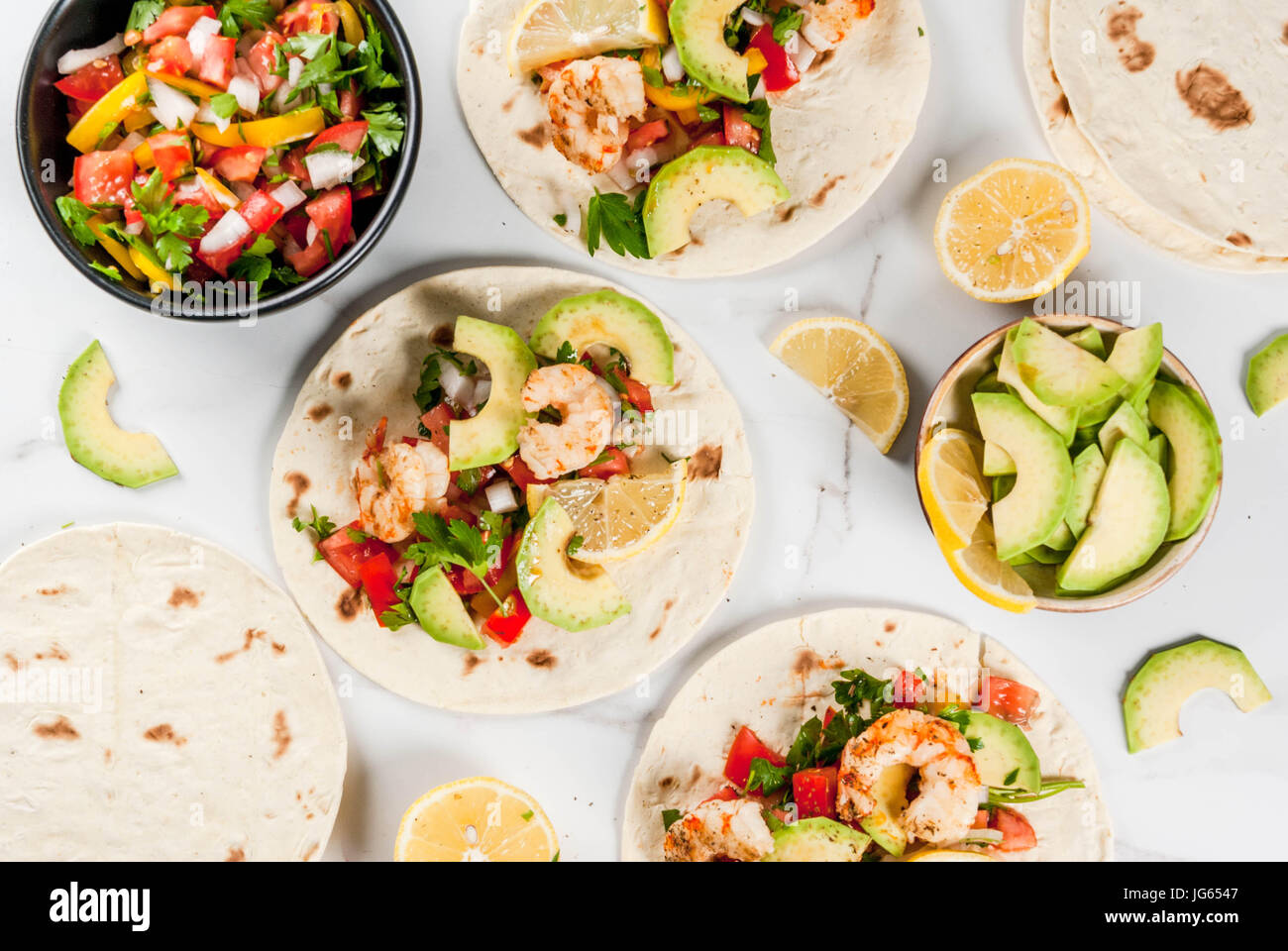 Seafood. Mexican food. Tortilla tacos with traditional homemade salsa salad, parsley, fresh lemon, avocado and grilled shrimp pawns. On a white marble Stock Photo