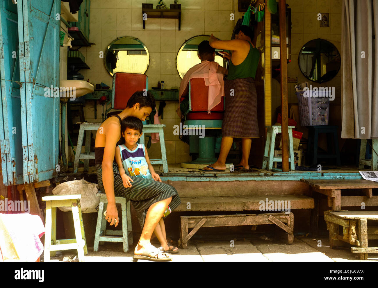 A boy waits to get his haircut at a barber shop in downtown Yangon, Myanmar Stock Photo