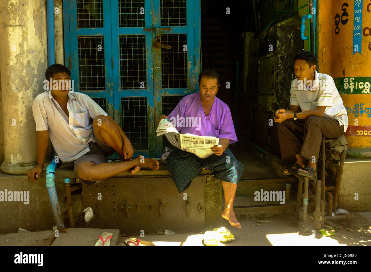 Three residents share a newspaper in downtown Yangon, Myanmar Stock Photo