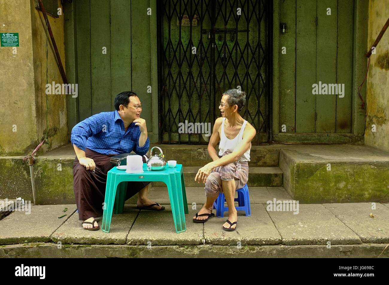 Two male residents have a discussion over tea in a street in downtown Yangon, Myanmar Stock Photo