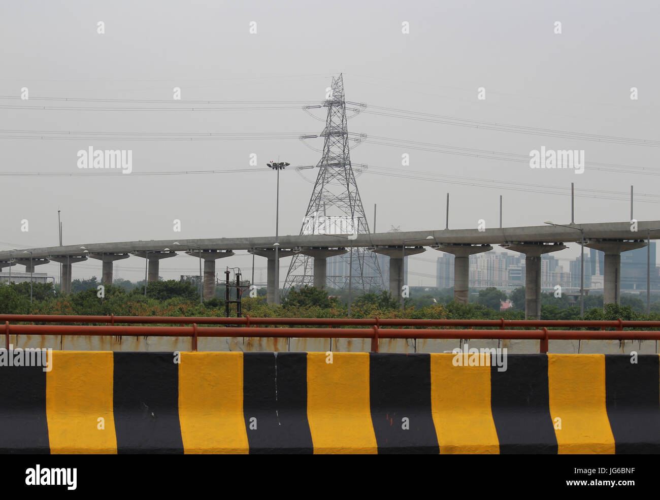 Elevated metro rail line being laid in Greater Noida. High tension line and buildings visible behind it. Photograph taken from Yamuna e-way Stock Photo