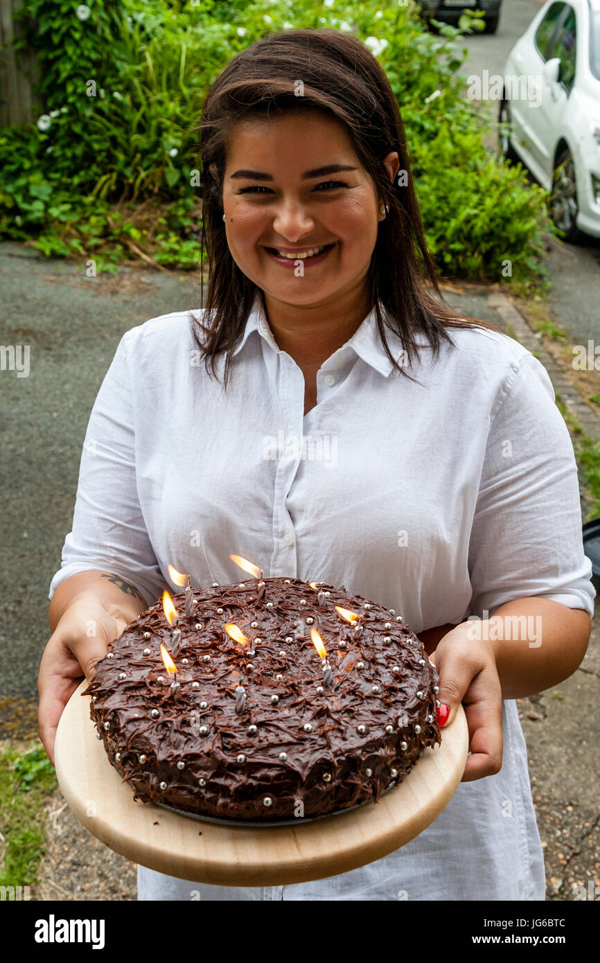 A Young Woman Standing On A Doorstep Holding A Birthday Cake, Sussex, UK Stock Photo