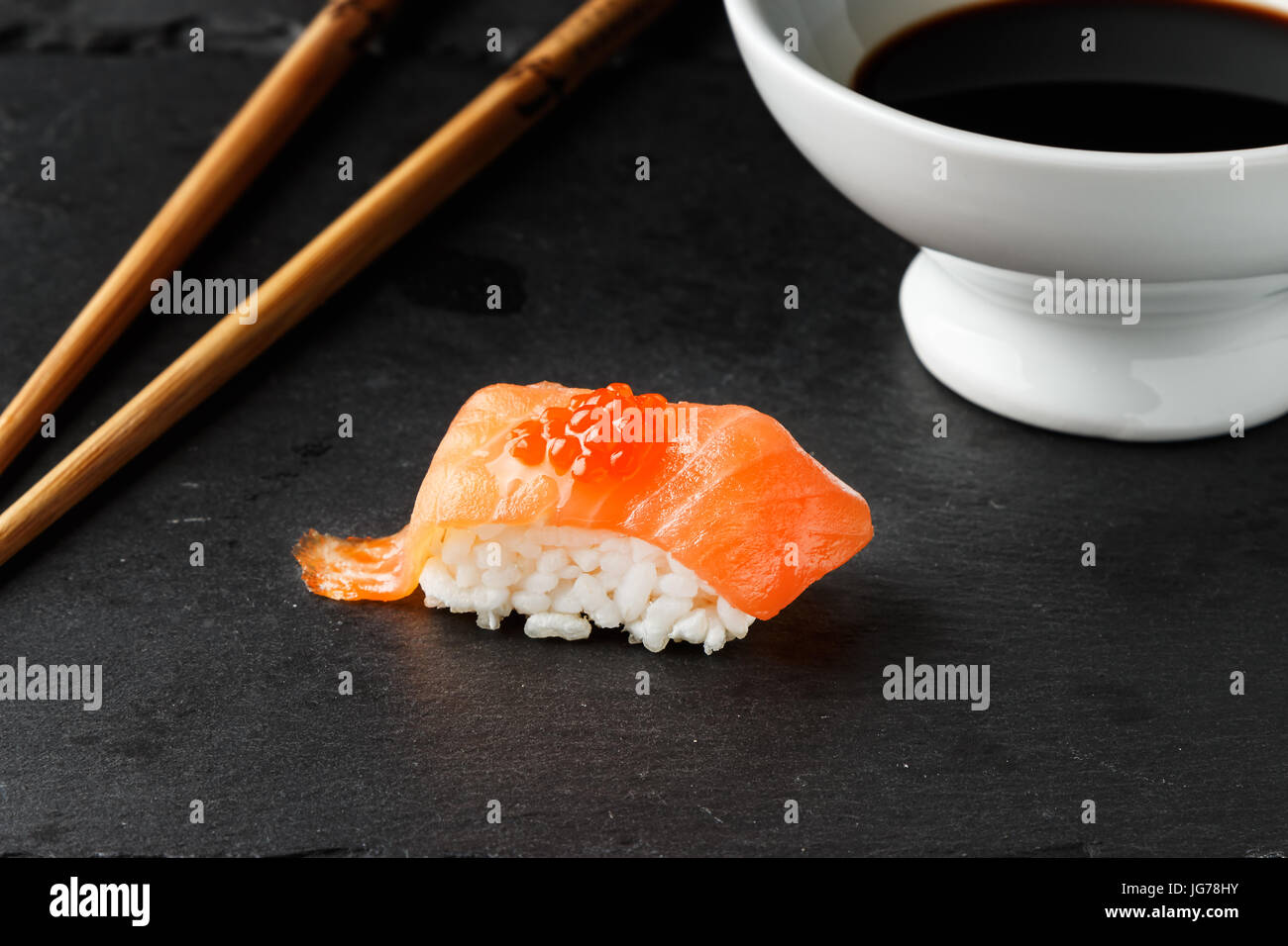 Salmon Nigiri with salmon roe on black slate stone with chopsticks and bowl of soy sauce. Raw fish in traditional Japanese sushi style. Horizontal ima Stock Photo