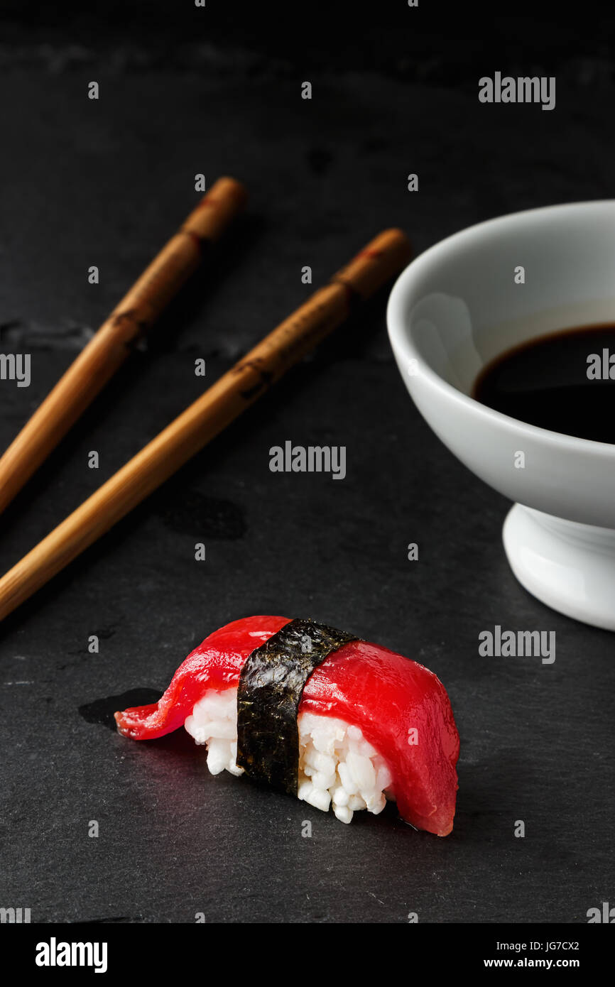 Red tuna Nigiri with Nori seaweedi on black slate stone with chopsticks and bowl of soy sauce. Raw fish in traditional Japanese sushi style. Vertical  Stock Photo