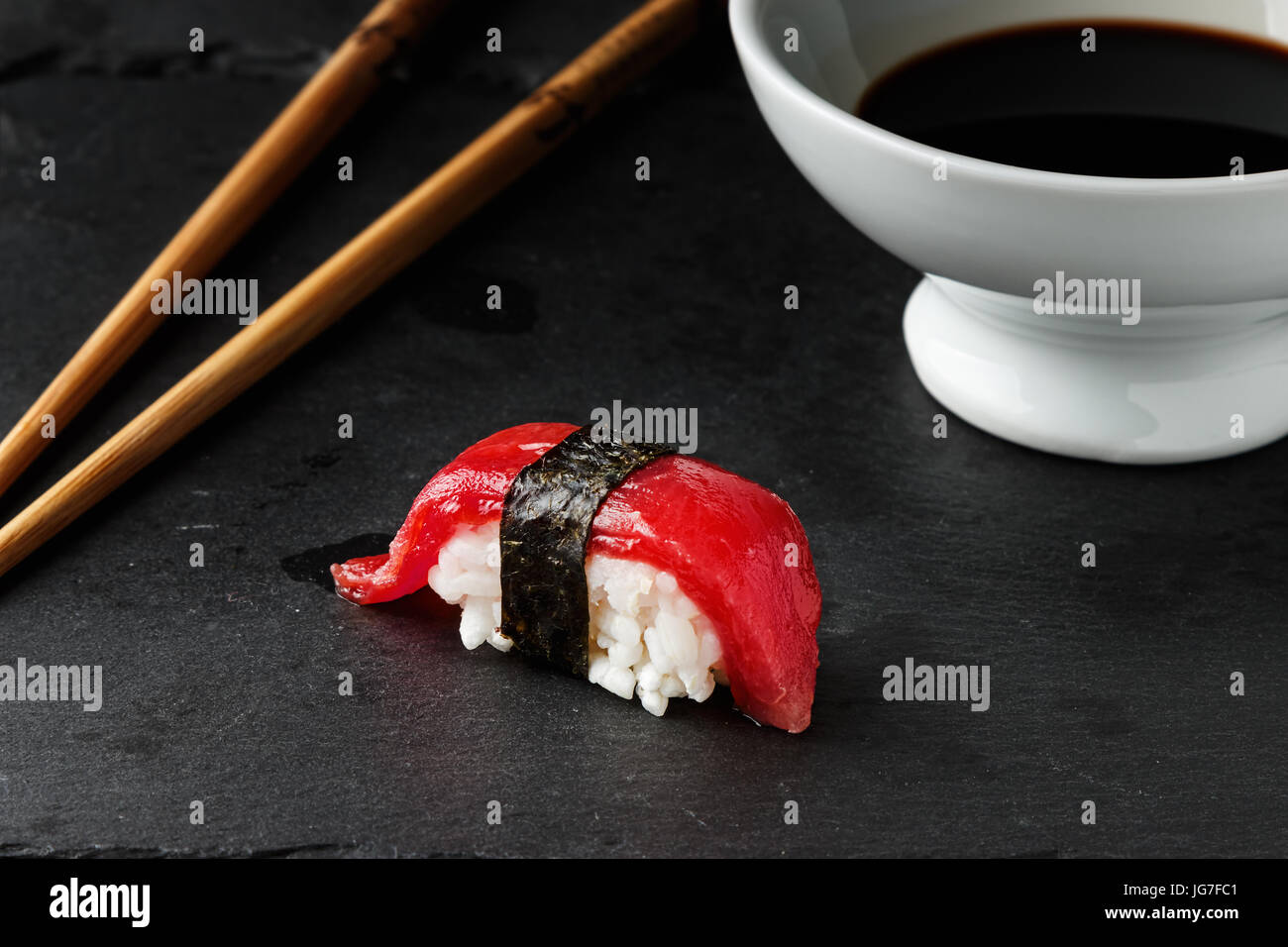 Red tuna Nigiri with Nori seaweedi on black slate stone with chopsticks and bowl of soy sauce. Raw fish in traditional Japanese sushi style. Horizonta Stock Photo