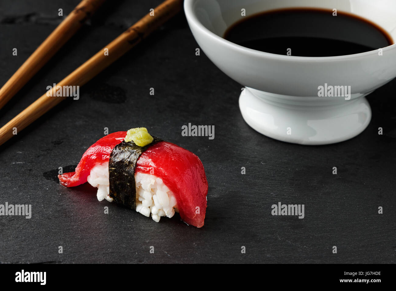 Red tuna Nigiri with Nori seaweed and wasabi paste on black slate stone with chopsticks and bowl of soy sauce. Raw fish in traditional Japanese sushi  Stock Photo