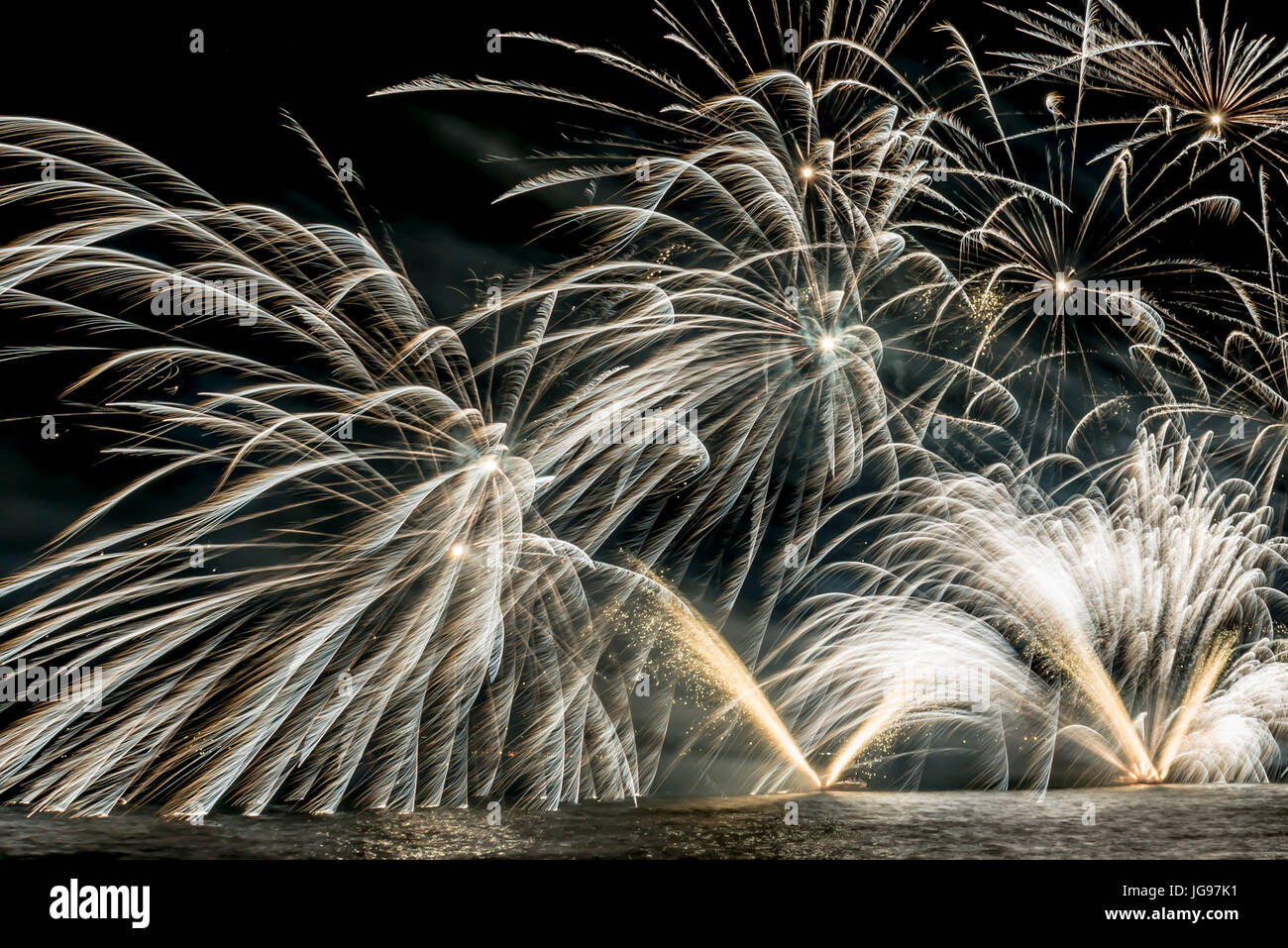 Details of Fireworks on the lakefront of Luino over the Maggiore Lake in a summer evening with blue sky and mountains in the background Stock Photo