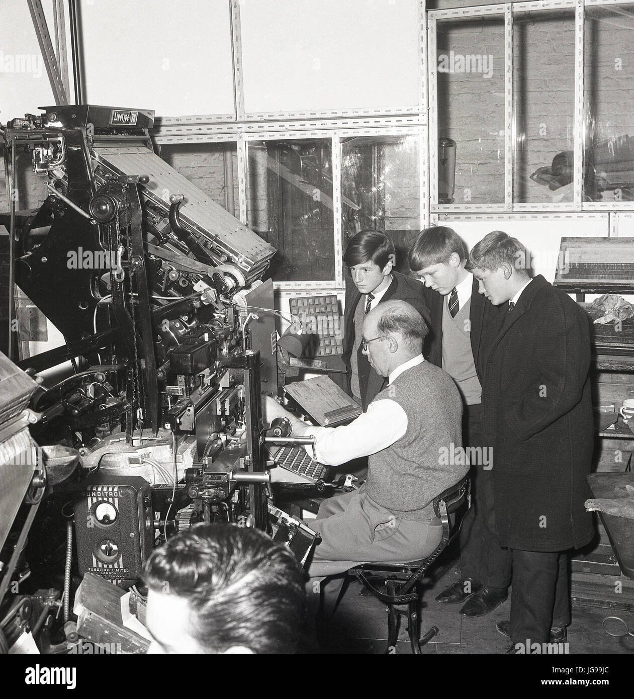 1960s, three school boys watch a newspaper typesetter or compositor at work on a visit to the printing presses of the South East London and Kentish Mercury newspaper, England, UK. Stock Photo