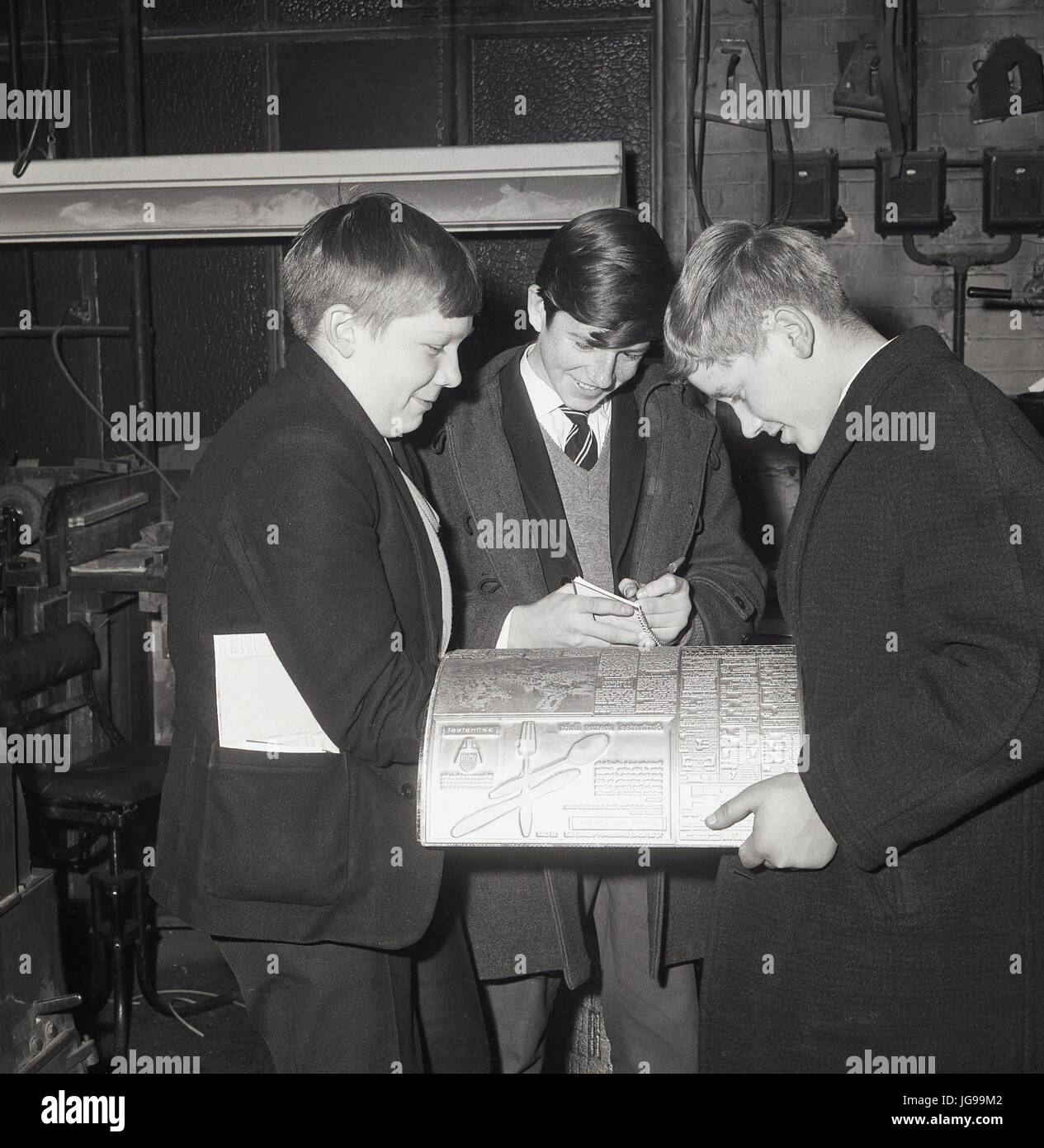 1960s, three school boys study a metal printing plate on a visit to the printing presses of the South East London and Kentish Mercury newspaper, England, UK. Stock Photo