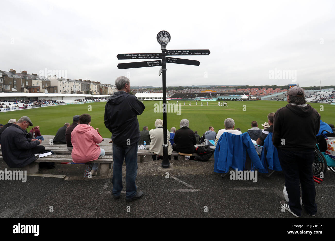 Fans watch the action by a signpost displaying how near the major county grounds are during the Specsavers County Championship, Division One match at the North Marine Road Ground, Scarborough. Stock Photo