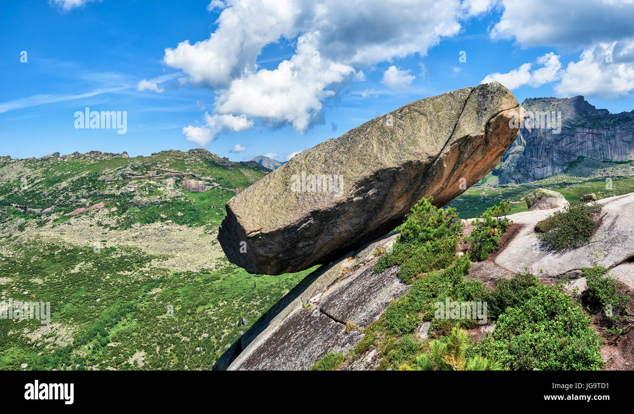 Hanging stone lies on sloping surface of mountain above precipice. A huge boulder of granite and syenite is supported by a small area on mountain. Erg Stock Photo