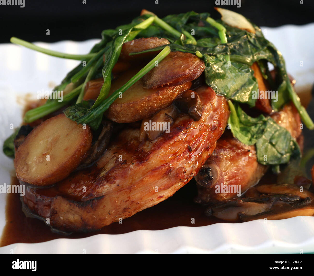Wilted spinach over pork chops with mushroom gravy and roasted potatoes on white ridged dish Stock Photo
