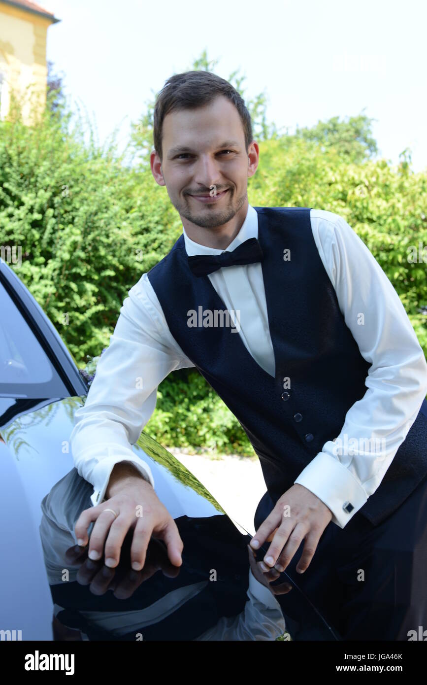 Groom smiling with wedding car Stock Photo - Alamy