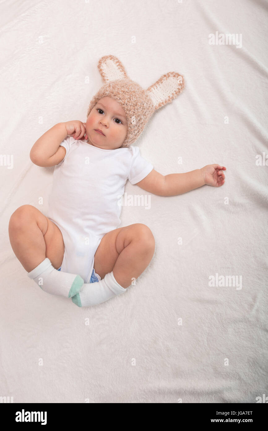 Cute baby boy in funny hat with ears lying on bed Stock Photo