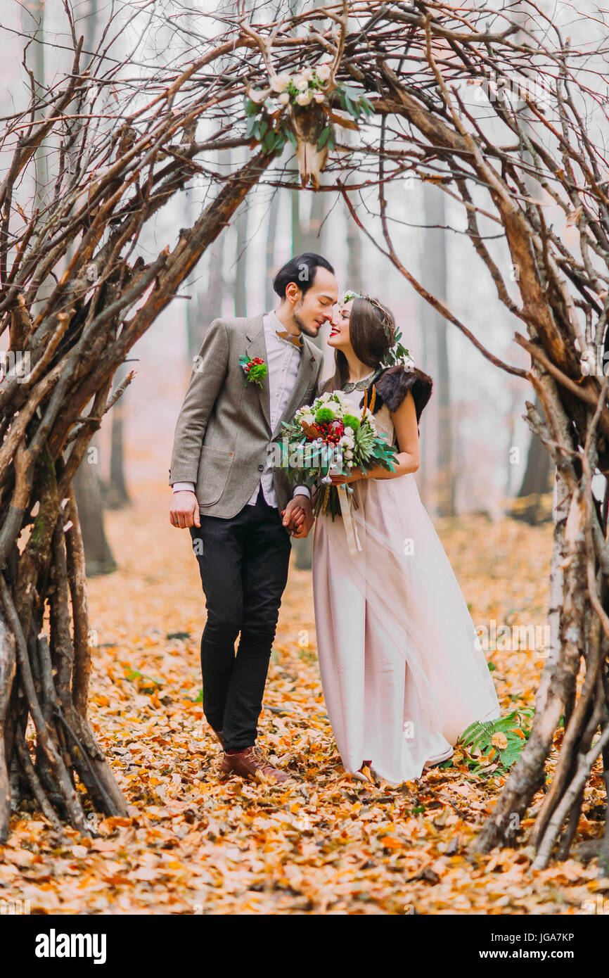 Wonderful wedding couple lovingly look at each other under the hazel arch in autumn forest Stock Photo