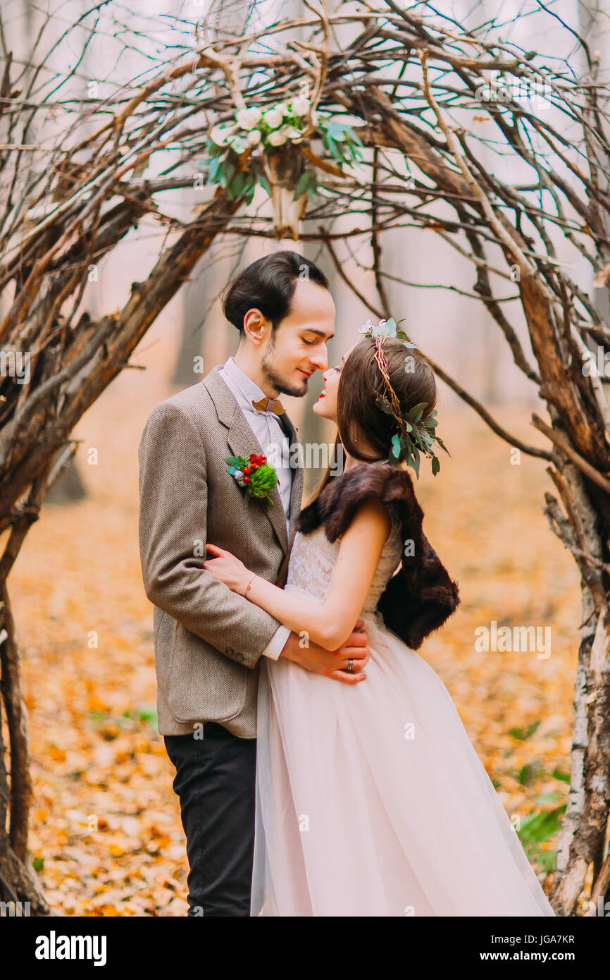 Charming stylish wedding couple softly hugging under romantic hazel arch in  autumn forest Stock Photo