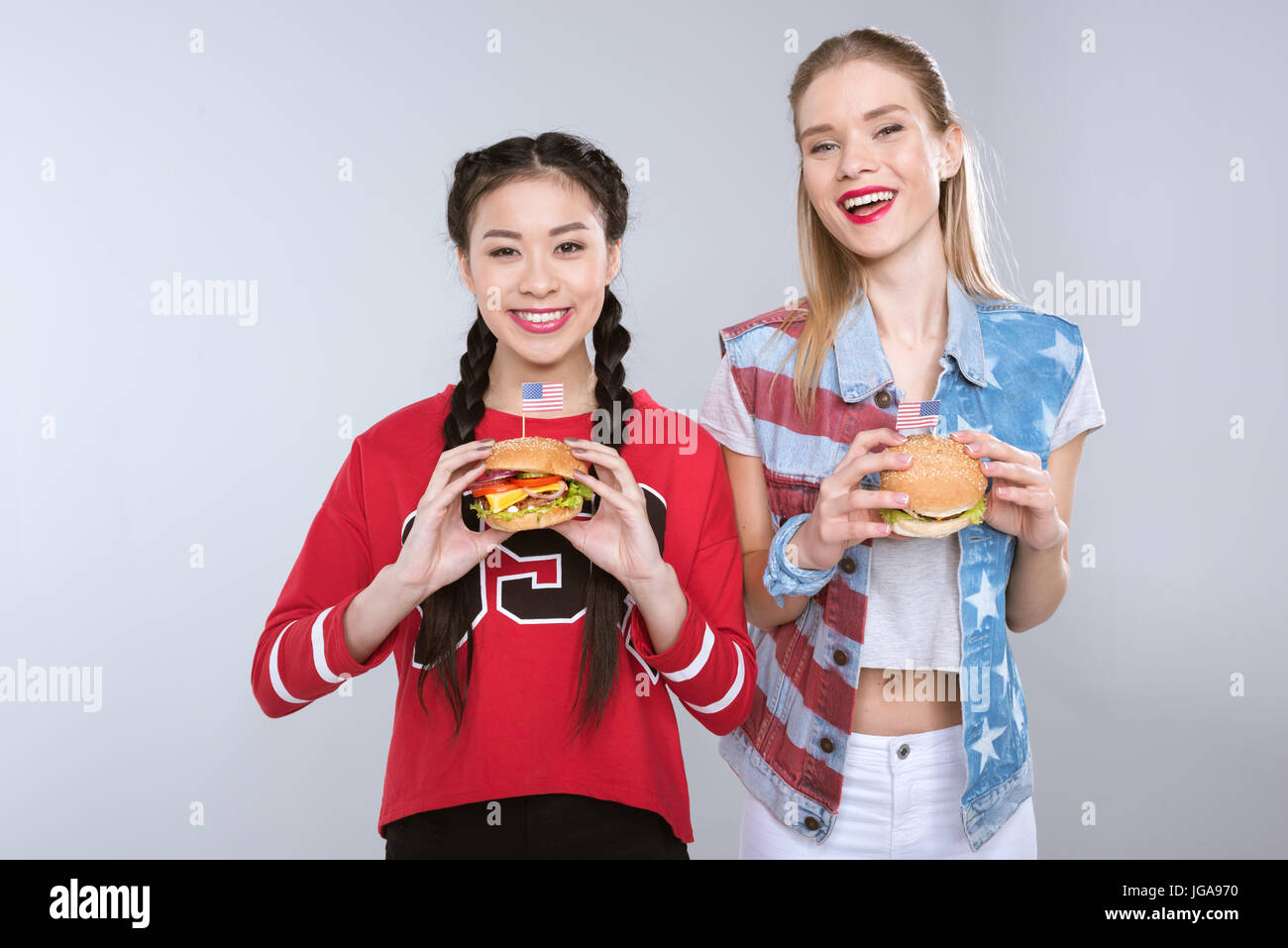 young smiling multiethnic girls holding burgers with USA flags, Independence Day Celebration Stock Photo