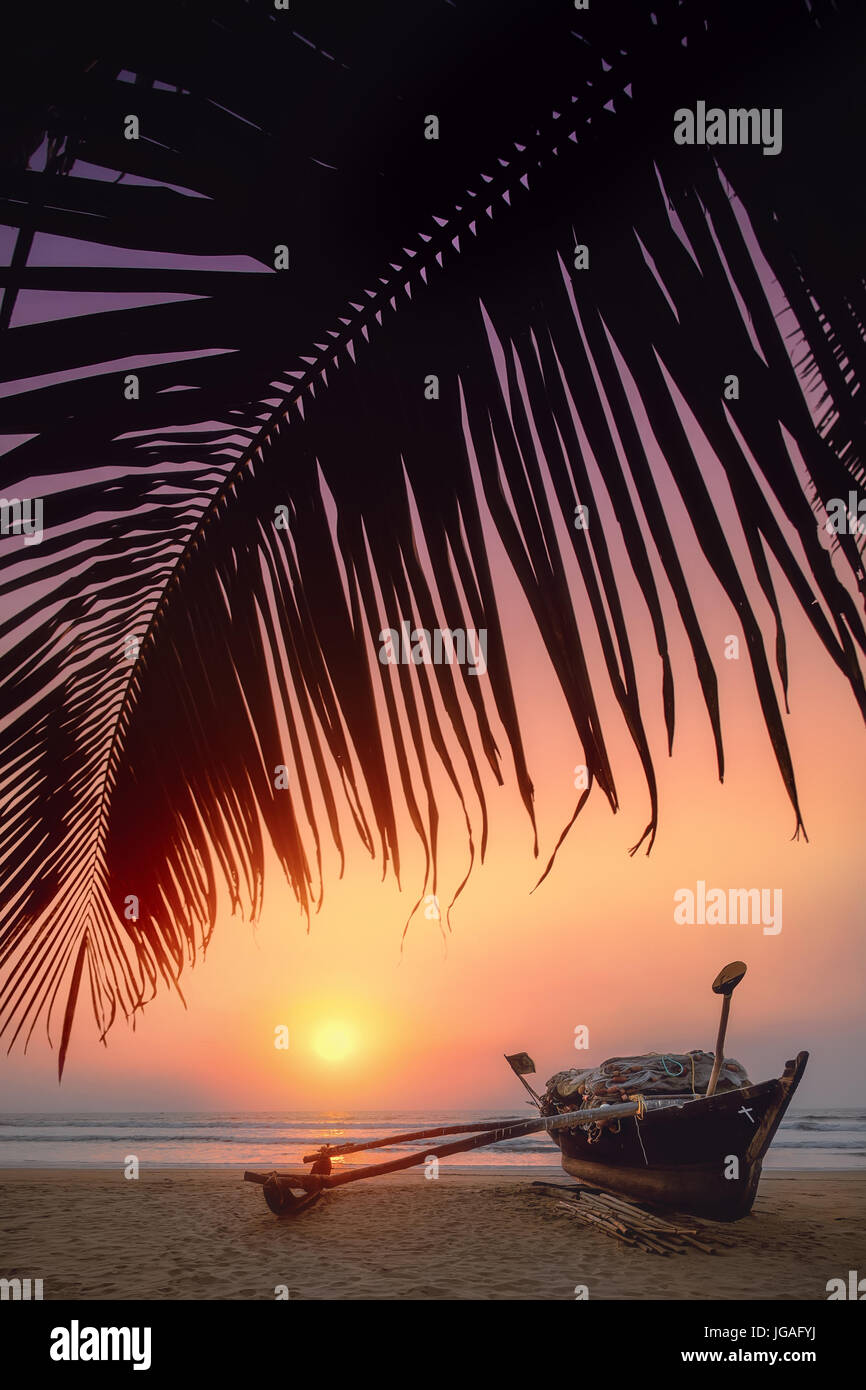 Beautiful sunset with a boat under the palm leaf on the beach. Stock Photo