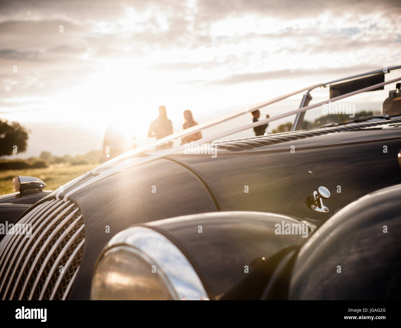 A close up of a Morgan car withh wedding ribbons on it late in the evening with sun flare and out of focus people in he background Stock Photo
