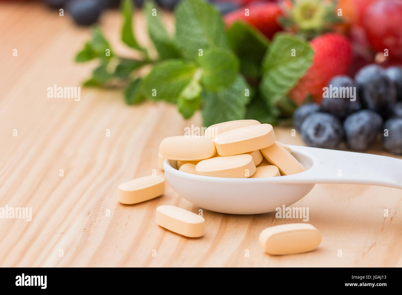 Multivitamin and supplement in a spoon and on wooded table with fruit and vegetables in the background. Stock Photo