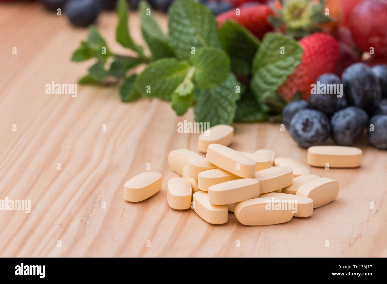 Multivitamin and  nutritional Supplement in a bottle and on wooded table with fruit and vegetables in the background. Stock Photo