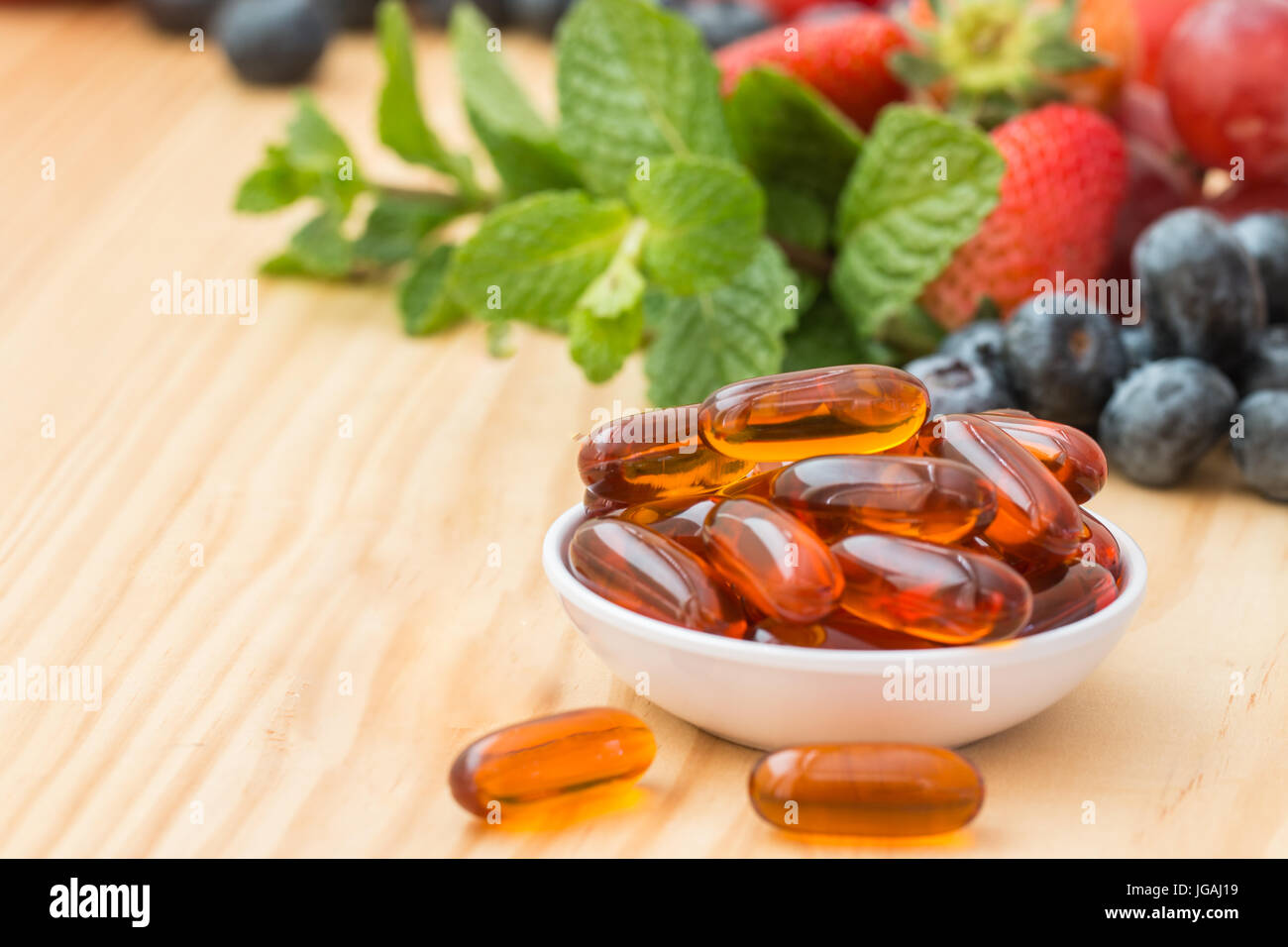 Lecithin gel vitamin supplement capsules in a cup and on wooded table with fruit and vegetables in the background. Stock Photo