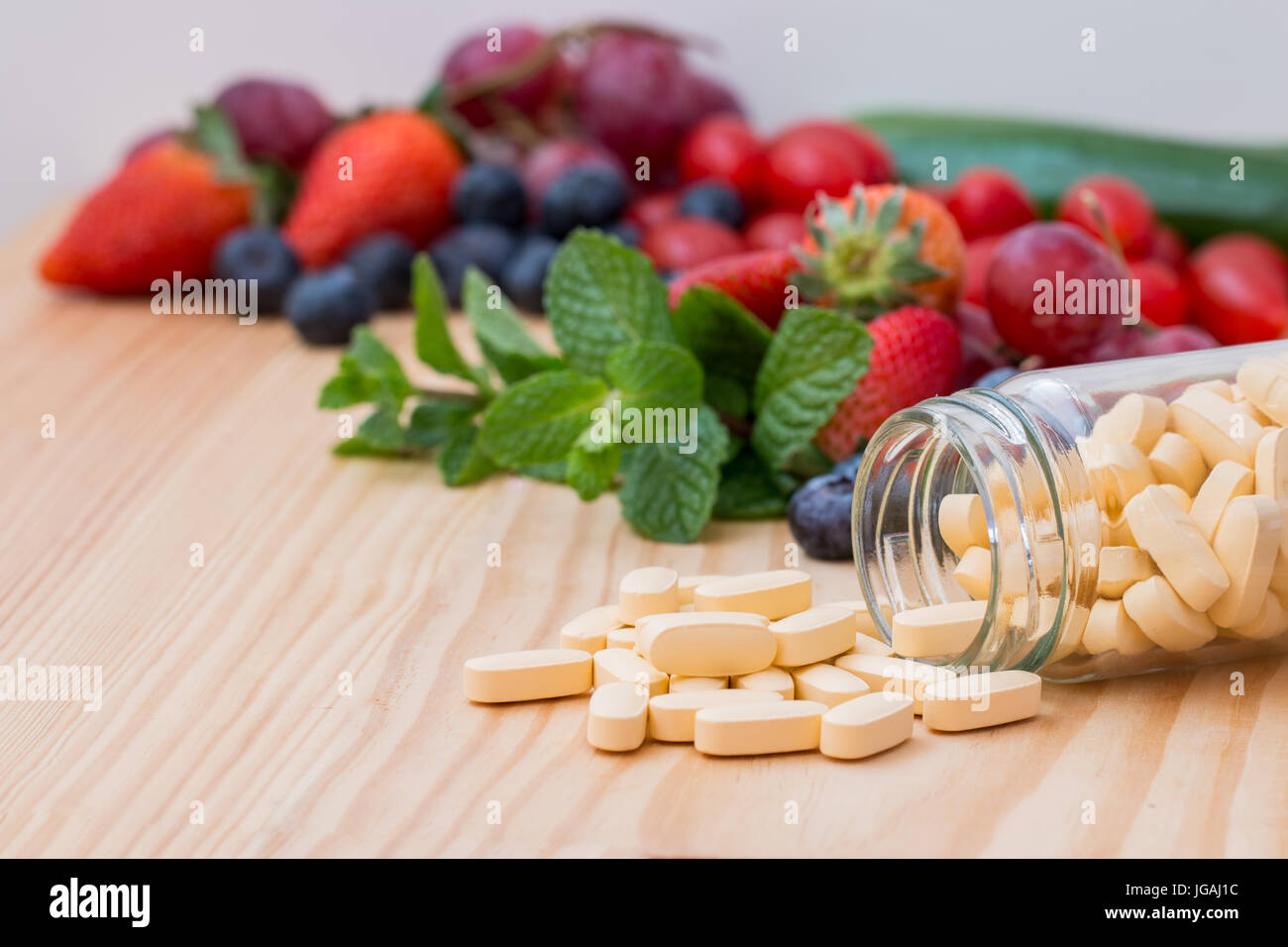 Multivitamin and nutritional Supplement in a bottle and on wooded table with fruit and vegetables in the background. Stock Photo