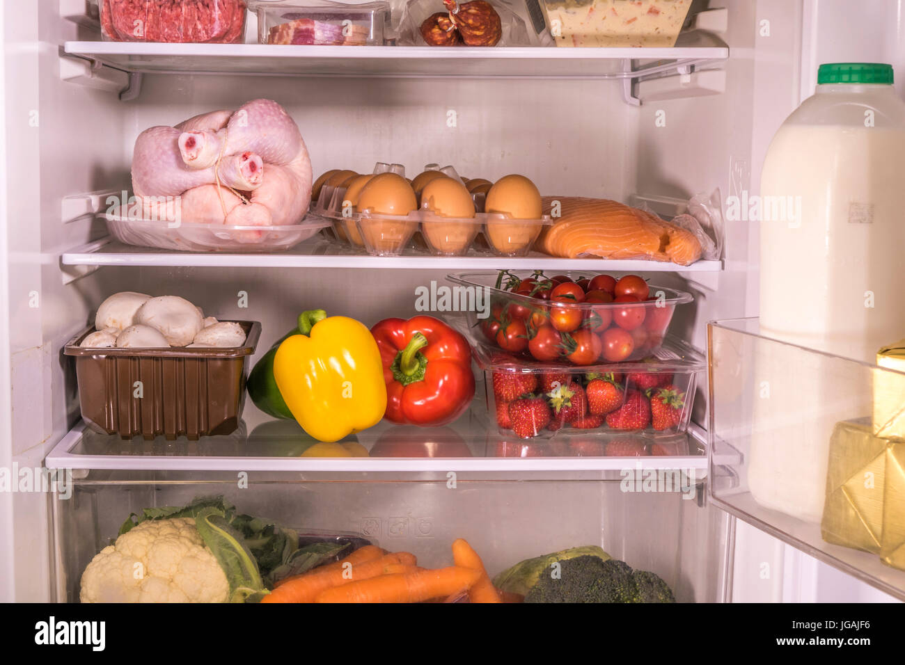 An open fridge with various items of fresh food and drink on the glass shelves. England, UK. Stock Photo