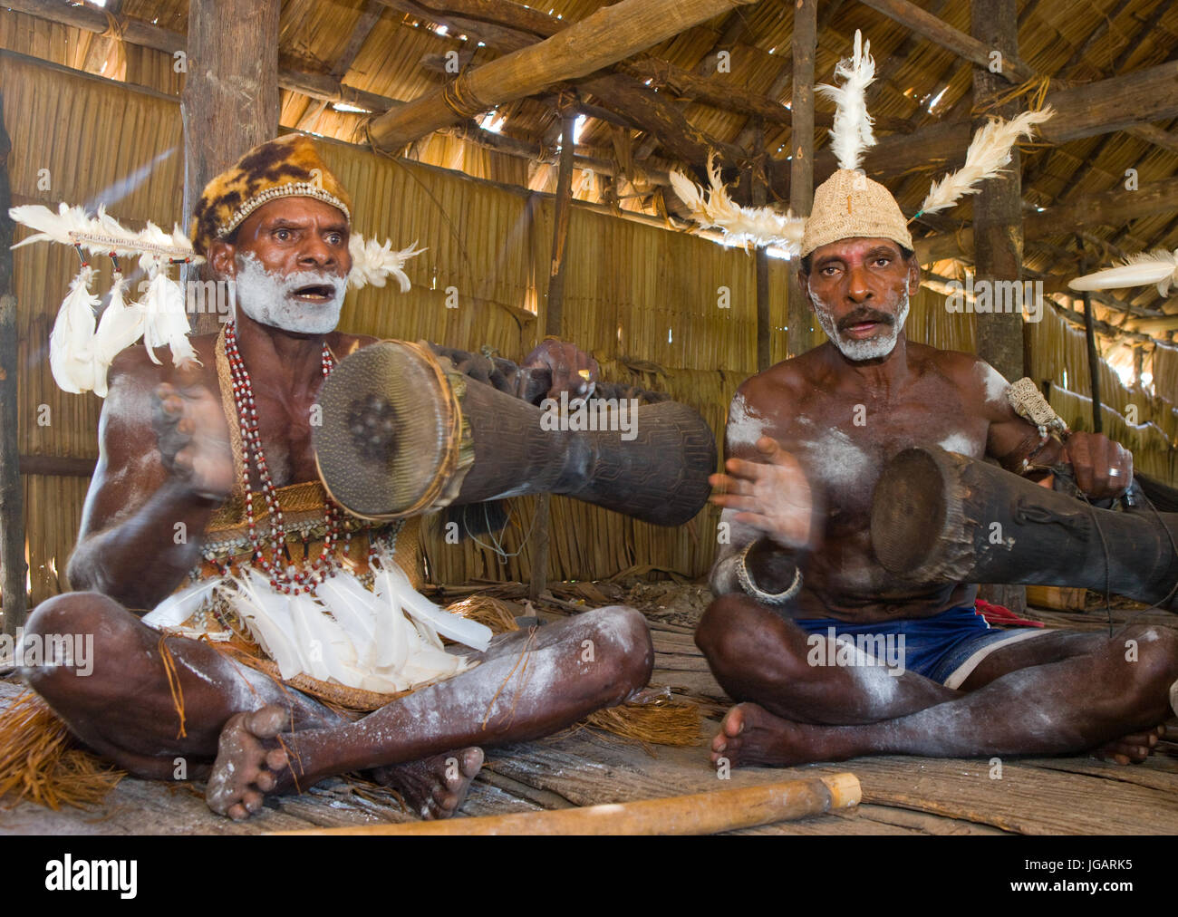 INDONESIA, IRIAN JAYA, ASMAT PROVINCE, JOW VILLAGE - JANUARY 19: Men Asmat tribe are sitting at home and play on the drum. Stock Photo