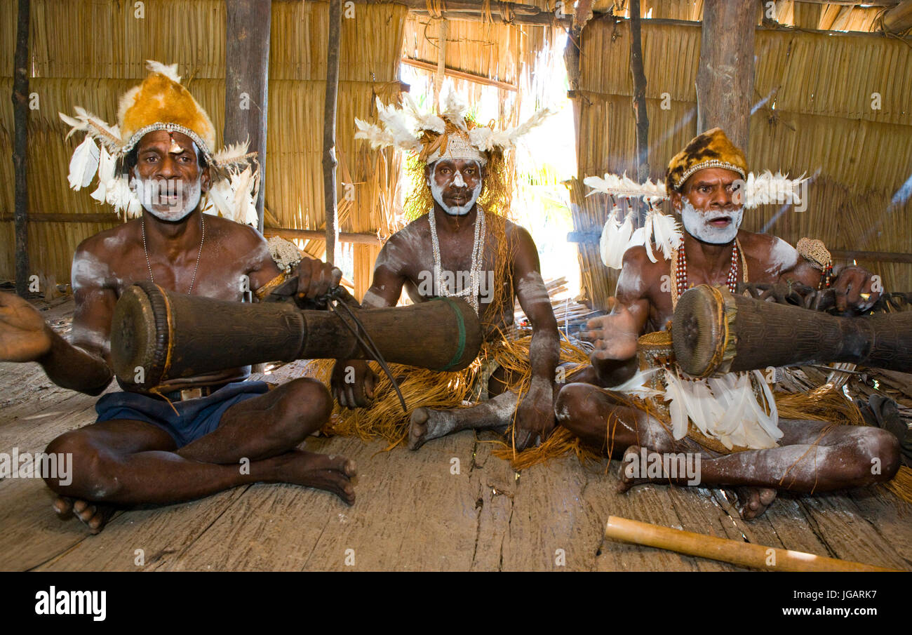 INDONESIA, IRIAN JAYA, ASMAT PROVINCE, JOW VILLAGE - JANUARY 19: Men Asmat tribe are sitting at home and play on the drum. Stock Photo