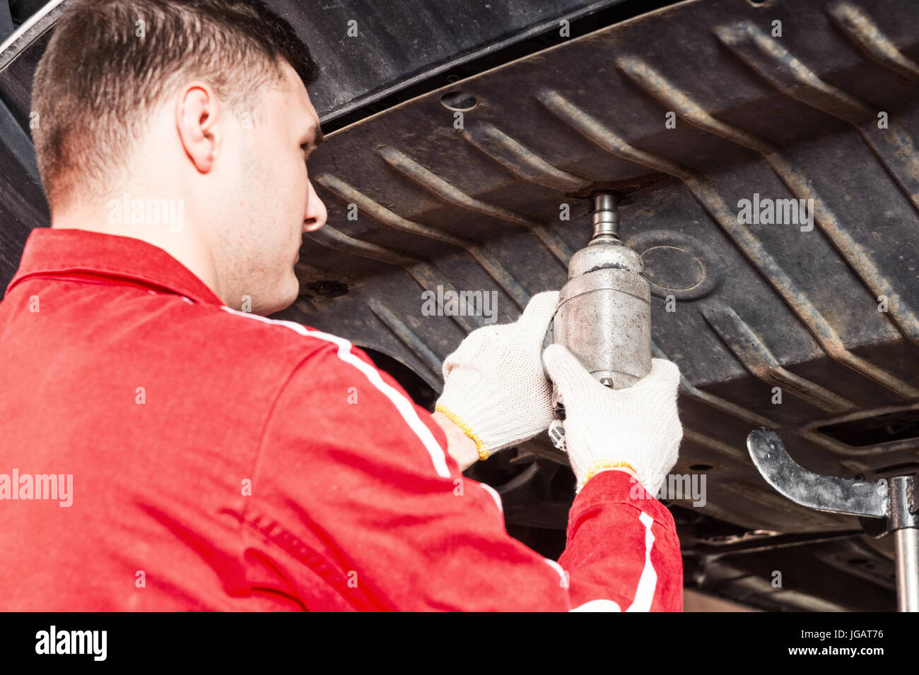 Professional young car mechanic in uniform working underneath a lifted