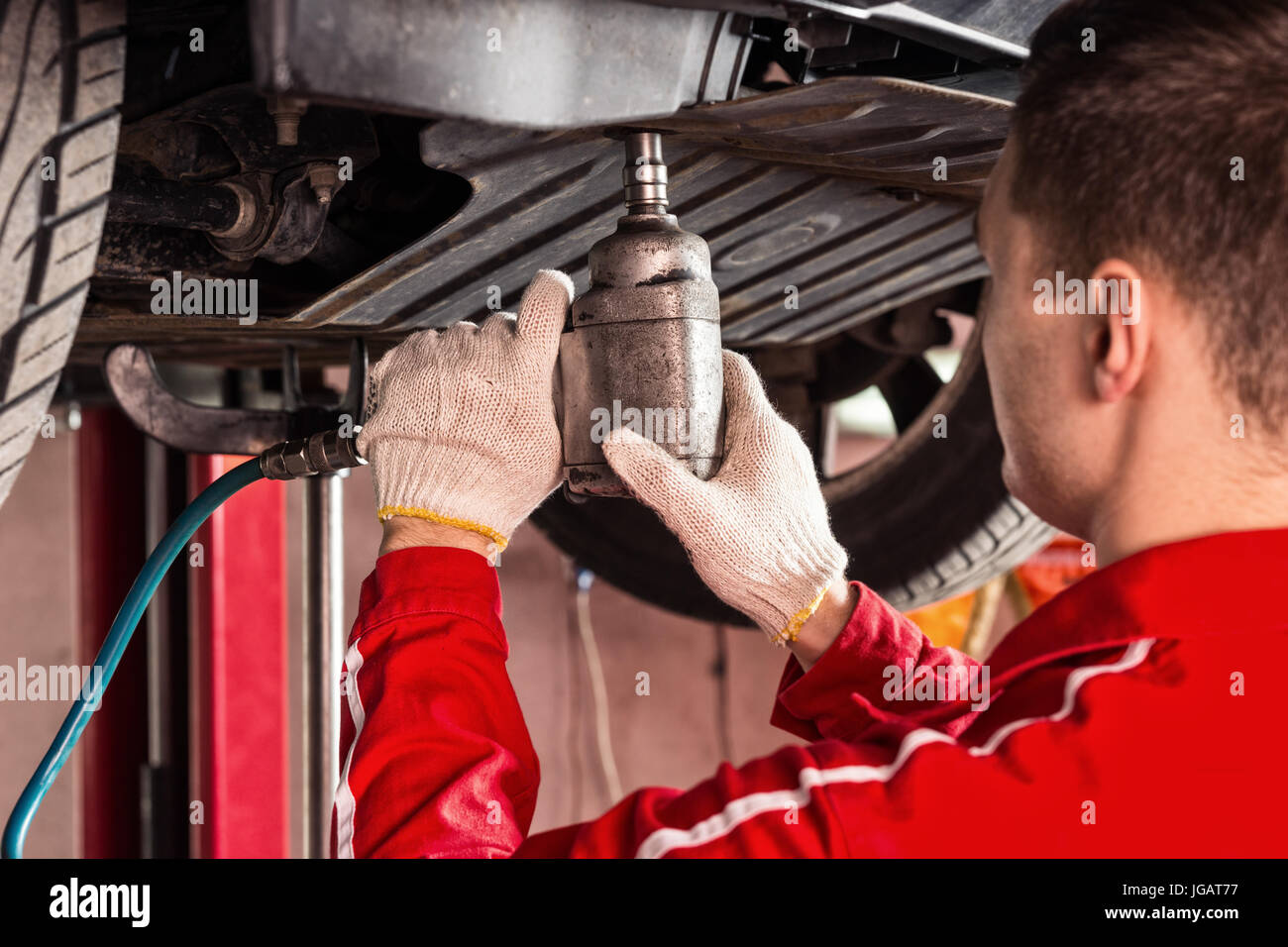 Professional male car mechanic in uniform working underneath a lifted
