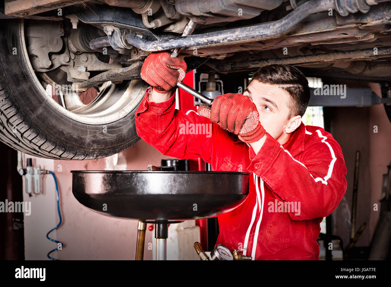 Male auto mechanic in uniform working underneath a lifted car and