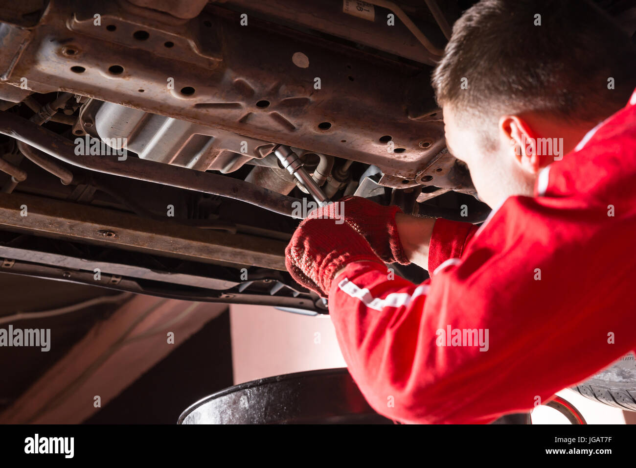Auto mechanic in uniform working underneath a lifted car and changing