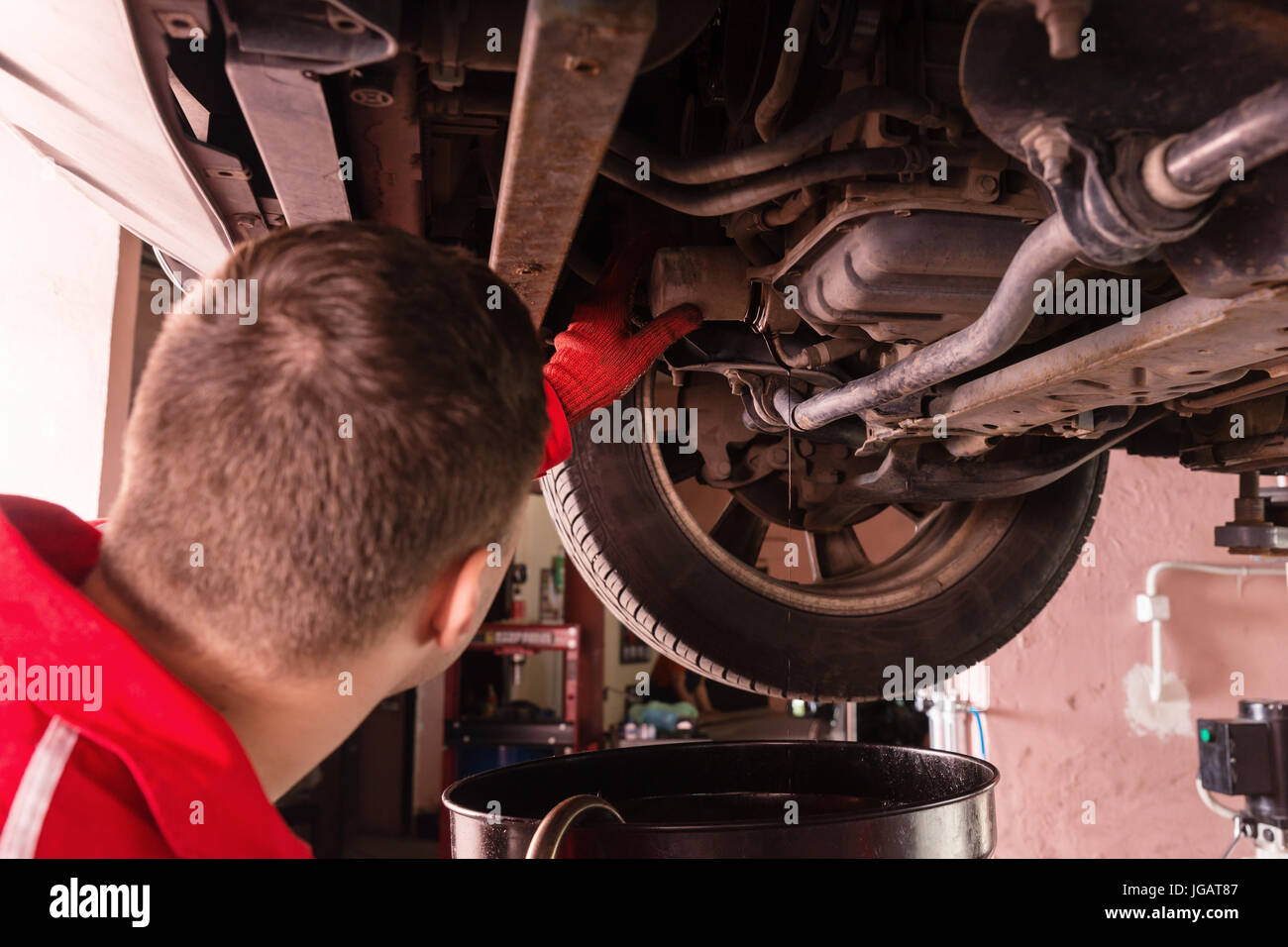Car mechanic in uniform working underneath a lifted car with working