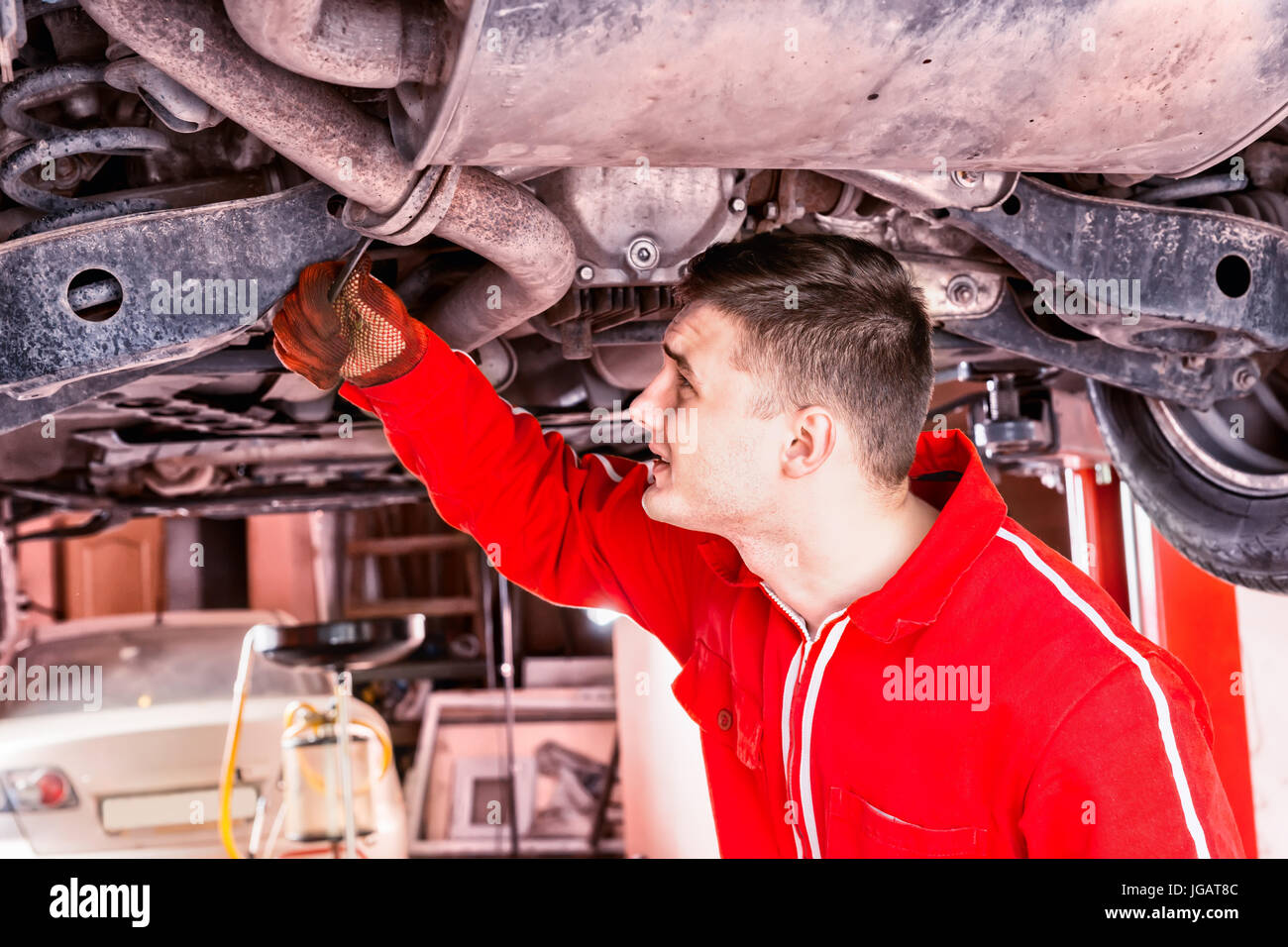 Mechanic in uniform working underneath a lifted car with working