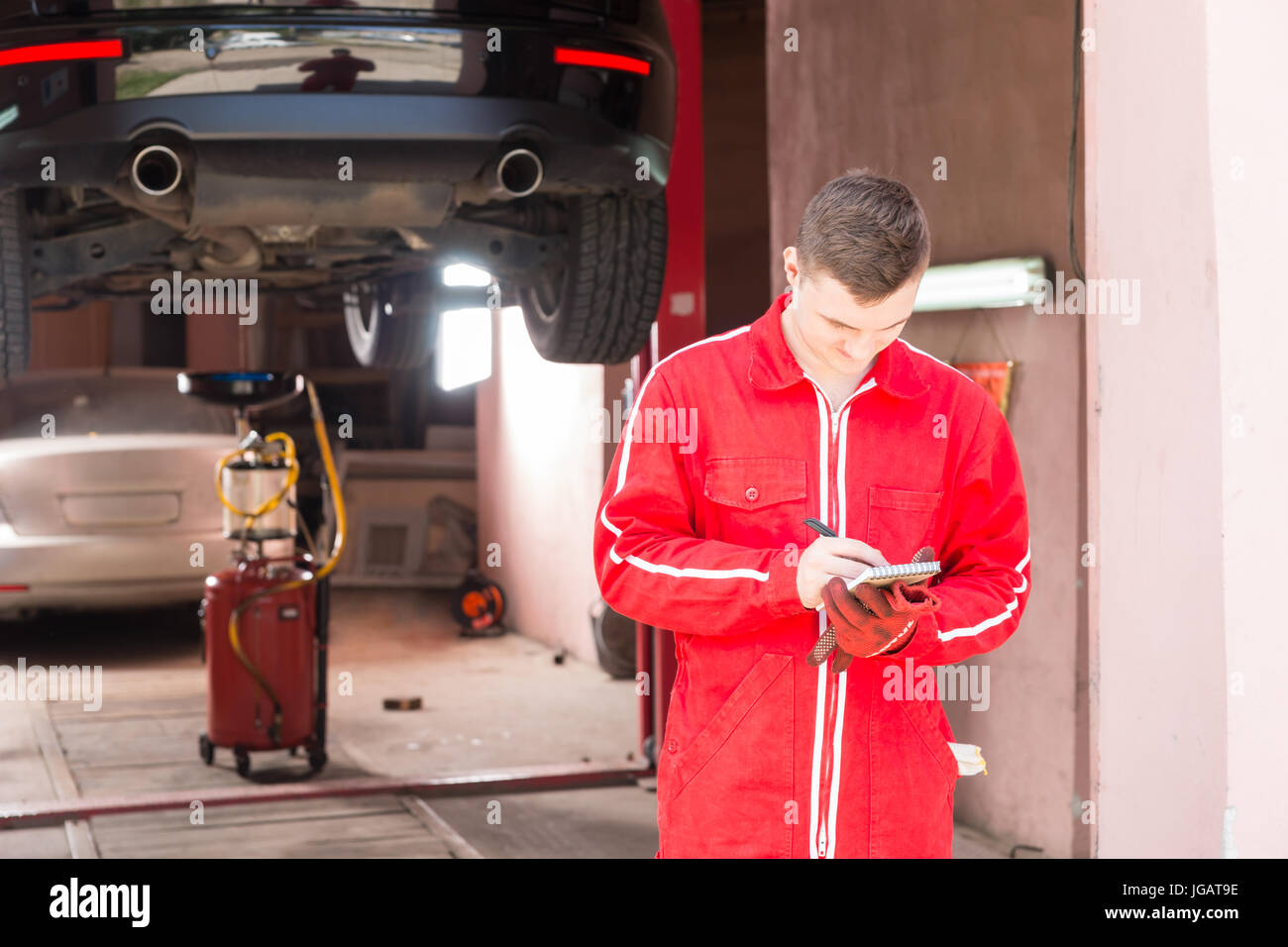 Male motor mechanic standing making notes in front of a black sedan ...