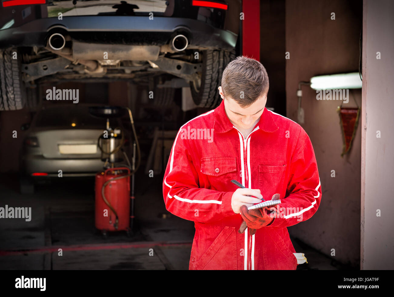 Motor mechanic standing making notes in front of a black sedan elevated ...