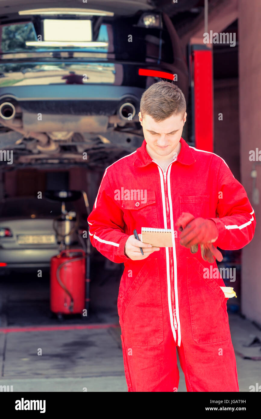Young male auto mechanic standing making notes in front of a black ...