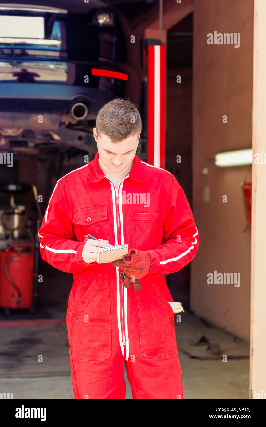 Male auto mechanic standing making notes in front of a black sedan ...