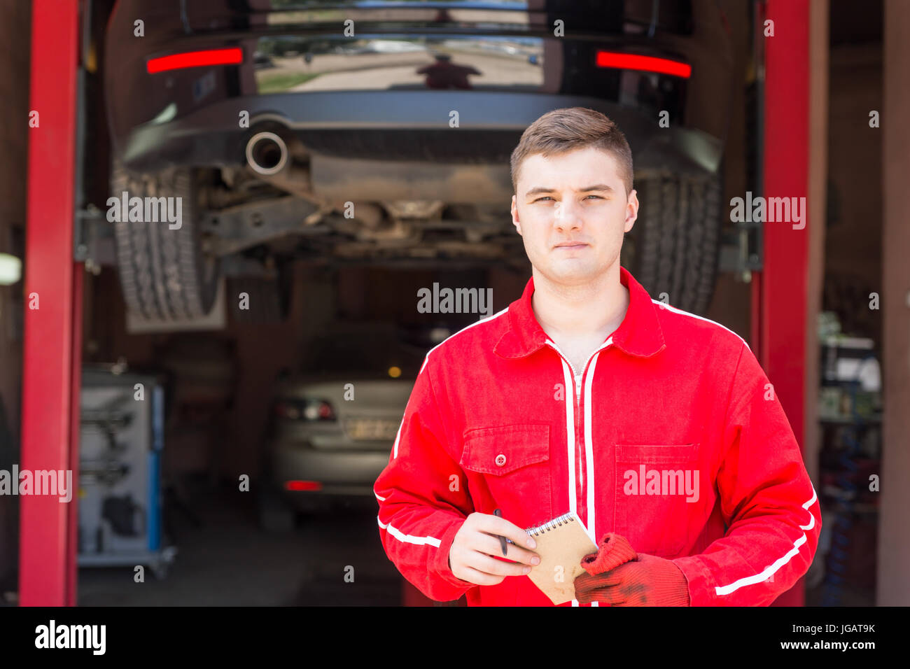 Serious male motor mechanic standing making notes in front of a black ...