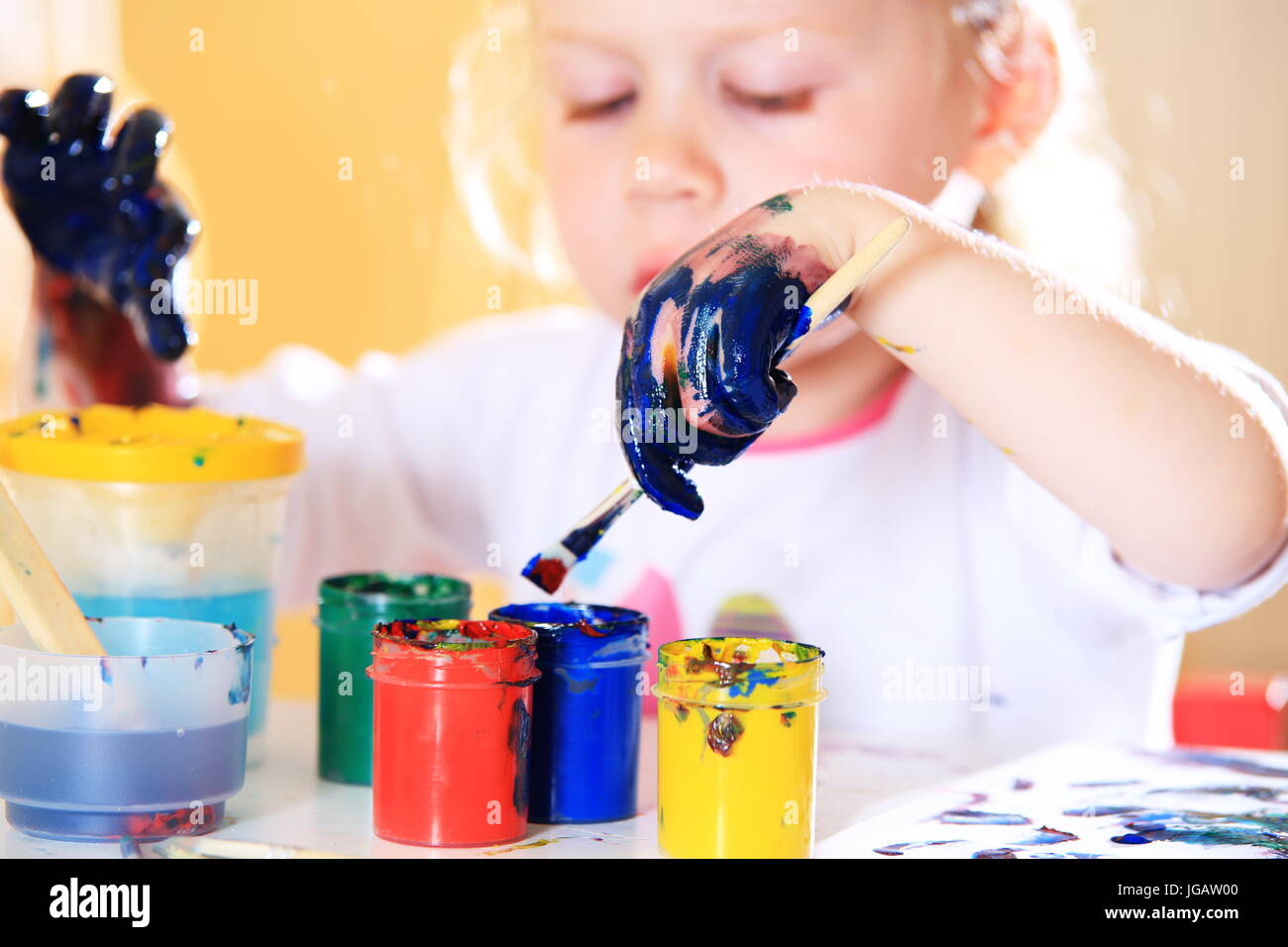 Girl with colorful paints close-up. Kid hands in blue paint. White little girl try draw with brush. Stock Photo