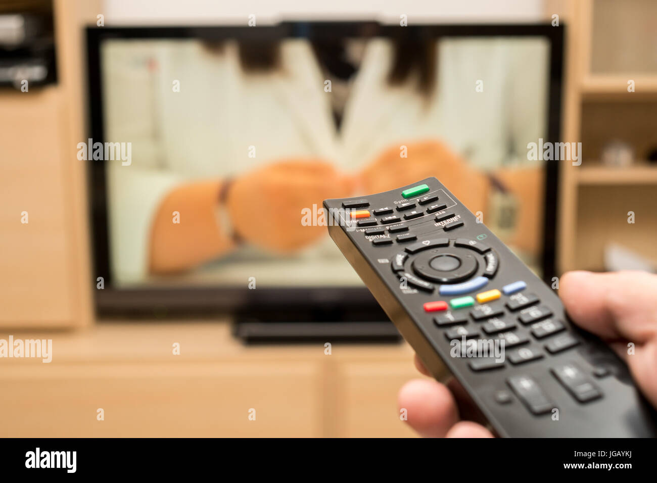 Watching TV and using black modern remote controller. Hand holding TV ...