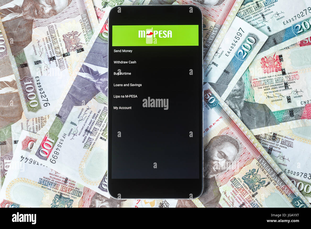 Safaricom M-Pesa fintech microfinance money transaction service on phone with Kenyan Shilling bank notes background Stock Photo