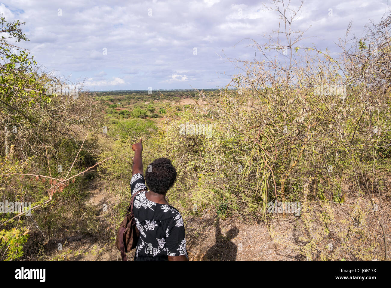 African woman pointing ahead to undeveloped countryside, Kenya Stock Photo