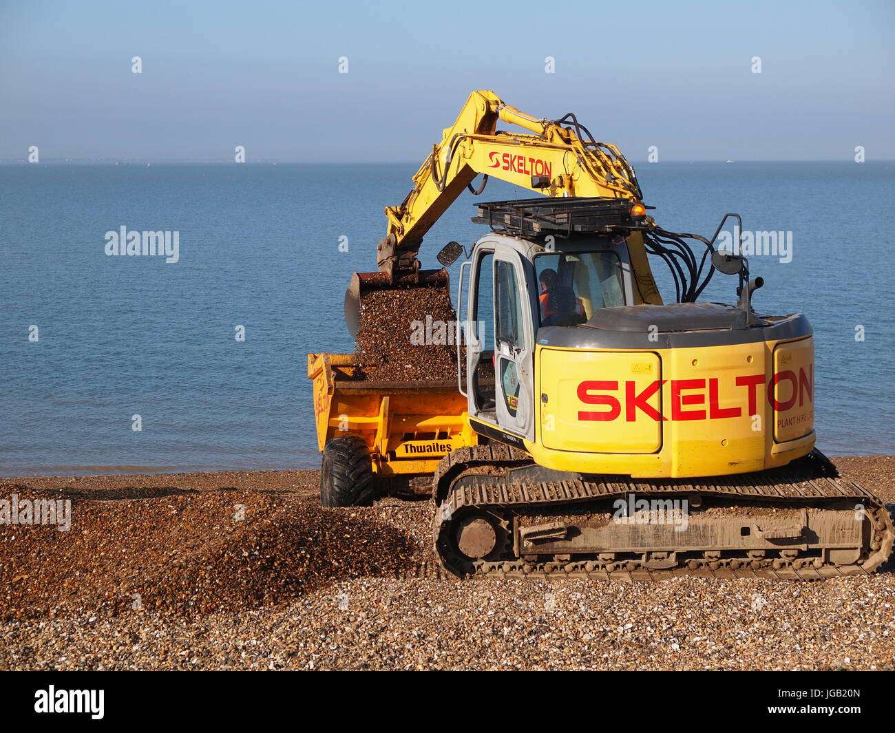 A small yellow tracked crawler excavator working on a beach to move shingle, UK. Stock Photo
